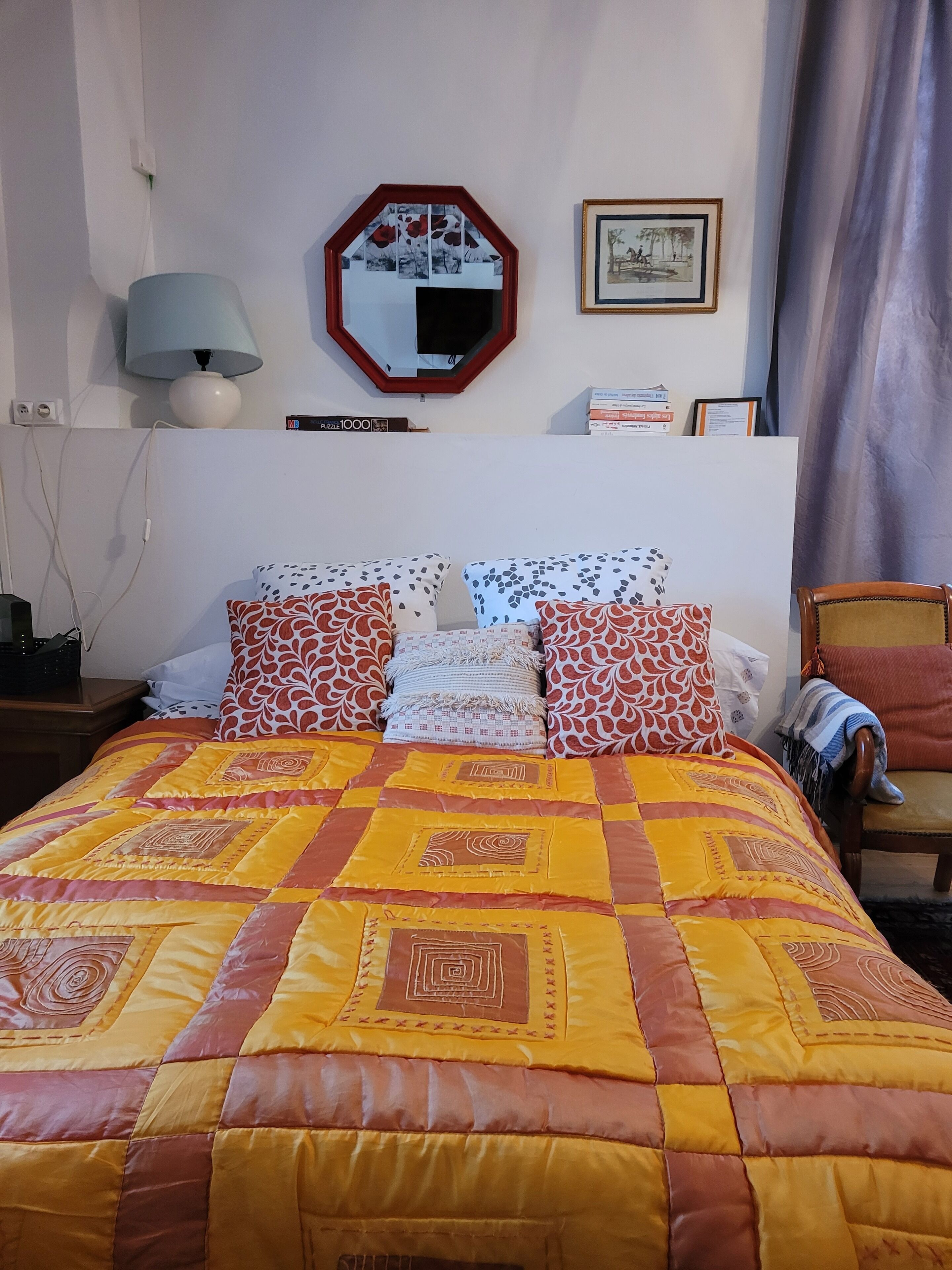 Une chambre à coucher avec un grand lit, un miroir, une lampe, une chaise et un tableau encadré au mur.