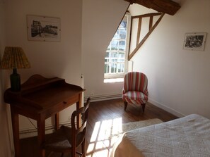 Una habitación con un escritorio de madera, un sillón a rayas, una cama con colcha estampada y dos cuadros enmarcados en las paredes.