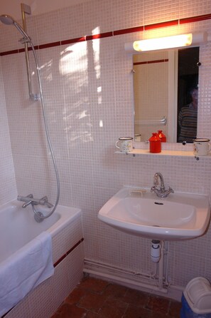 Bathroom features a white sink, bathtub, and showerhead, with a mirror above the sink and two shelves for storage.
