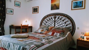 A neatly made bed with a patterned bedspread, a decorative headboard, and a bedside table with a lamp. - Welcome to U MERULU of "Vacances-a-moriani", a charming corsican apartment for 6 (San-Nicolao)