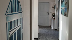 A hallway with a white door at the end, a wall with a nautical-themed mural, and a small cabinet with a vase of flowers. - Welcome to U MERULU of "Vacances-a-moriani", a charming corsican apartment for 6 (San-Nicolao)