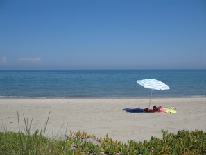 A beach with a person lying on a towel under a striped umbrella.