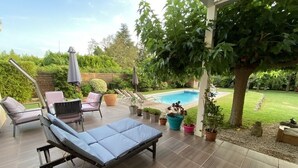 A covered patio with a pool, lounge chairs, and potted plants.
