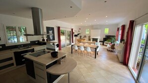 A modern kitchen with a central island, a dining area with a round table and chairs, and a living space with a fireplace.