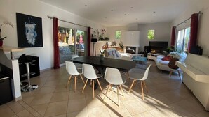 A spacious living area with a large dining table, white chairs, a sofa, and a TV.