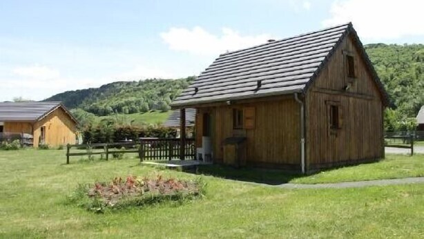 Une cabane en bois avec un toit en pente, entourée d’un champ herbeux et d’une clôture en bois.