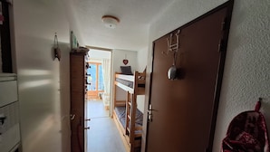 A narrow hallway with a wooden door on the right, a bunk bed in the background, and a small window with curtains. - Rental in Notre Dame de Bellecombe, Espace Diamant, 500m from the ski lifts.  (notre dame de bellecombe)