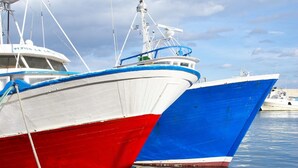 Twee boten aanmeren in een jachthaven, met kalm water en een bewolkte lucht.