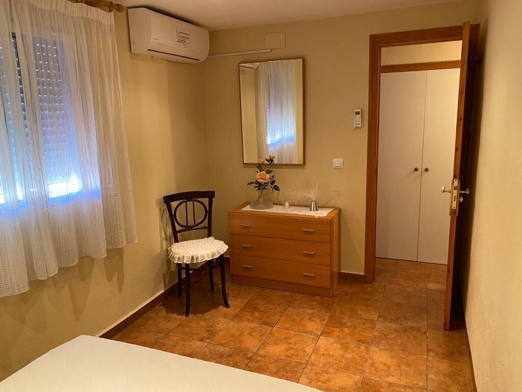 Una habitación con cama, una silla, cómoda, espejo y puerta.