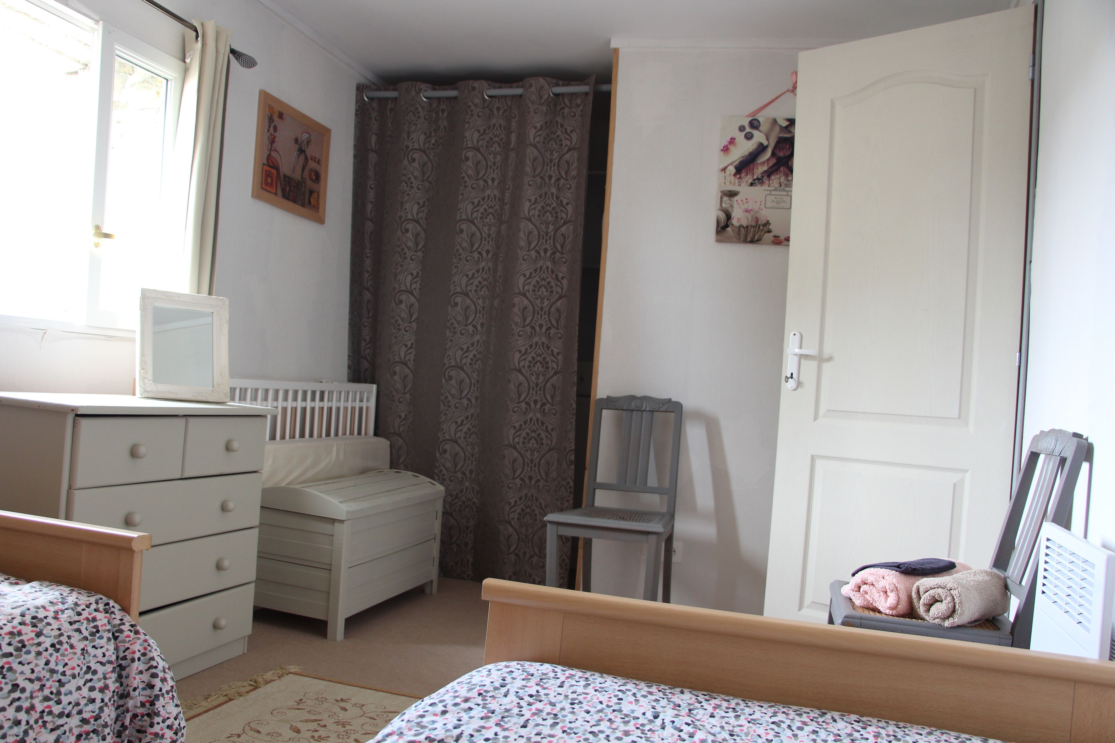 Quarto com cama, cômoda, cadeira, porta e janela com cortinas.
