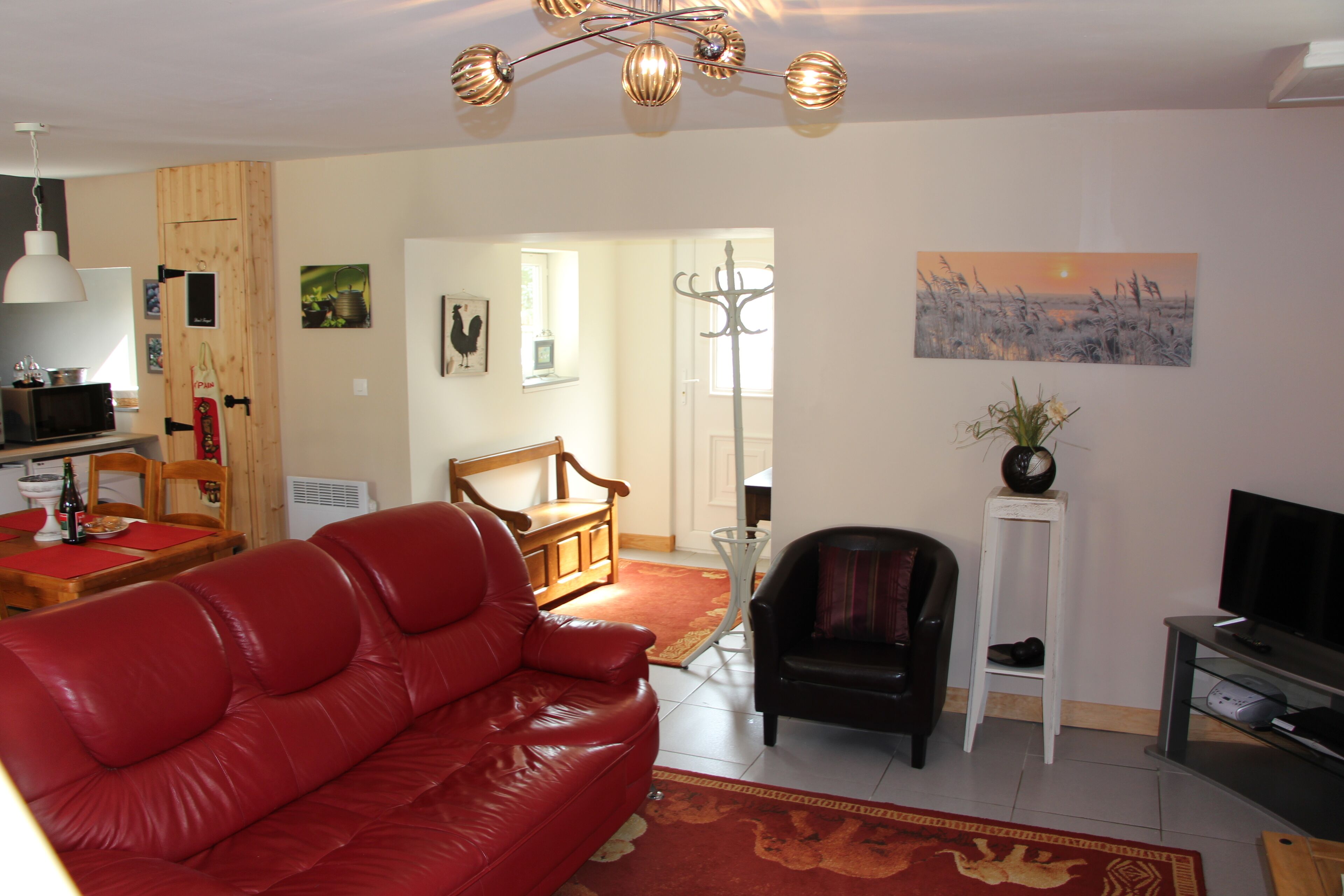 A living room with a red leather sofa, a black armchair, a TV stand, and a dining area with a wooden table and chairs.