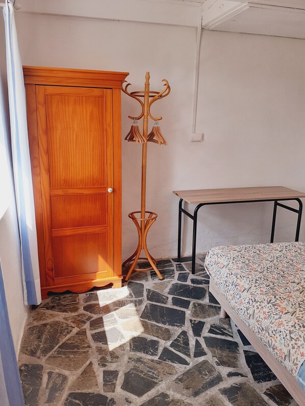 A room with a wooden wardrobe, a coat stand, a bed with a floral bedspread, and a tiled floor. - Ti Bihan at Pors Jaffrennou (Scrignac)