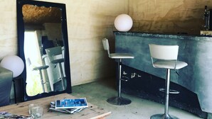 Ein rustikaler Raum mit Holzbalkendecke, einem großen Spiegel, zwei Barhocker, einem Holztisch mit Zeitschriften und einer Bar.