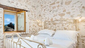 Een slaapkamer met een stenen muur, een bed met witte lakens, een raam met uitzicht en een plafondventilator.