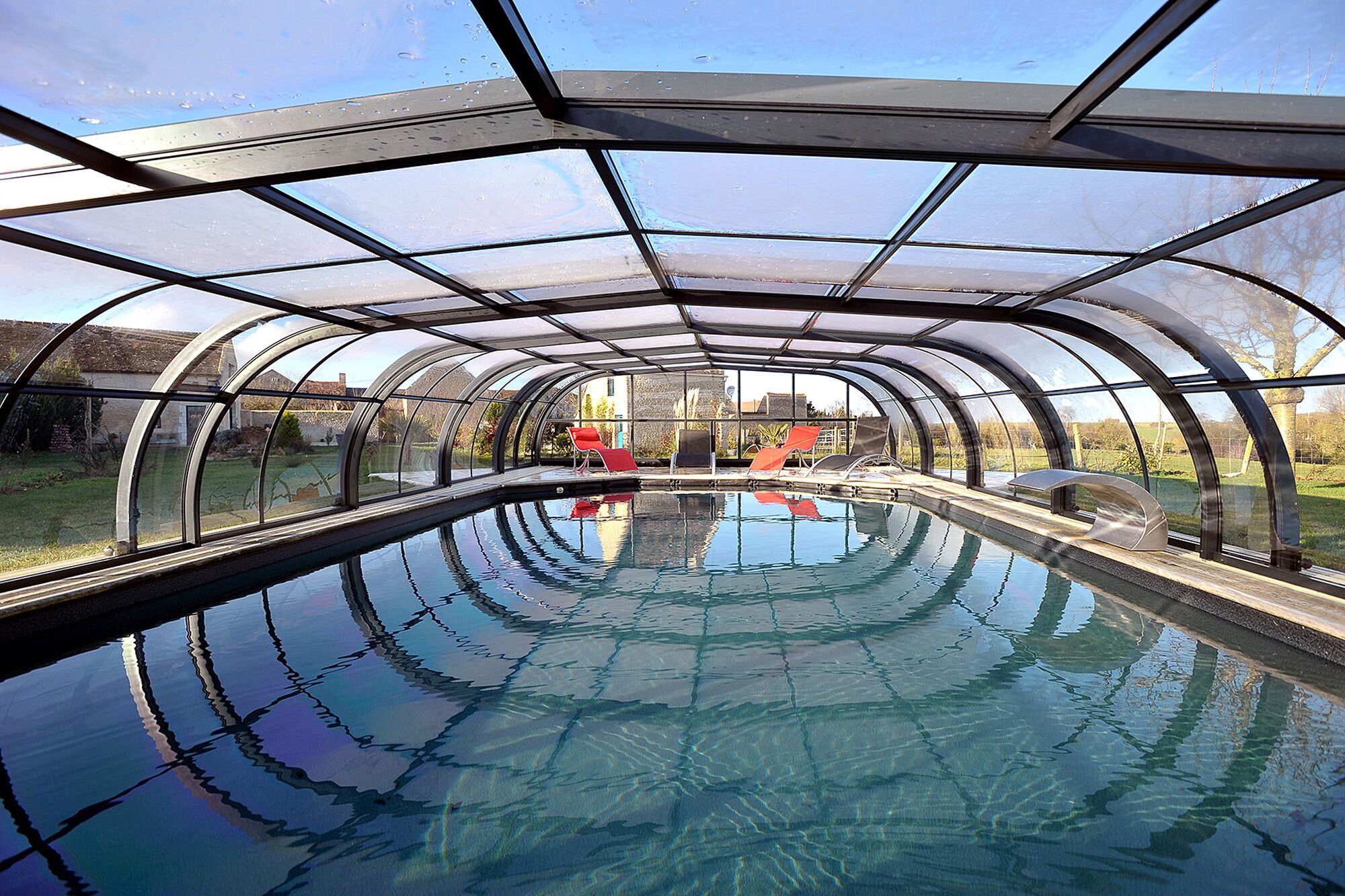 A transparent greenhouse structure with a swimming pool inside.