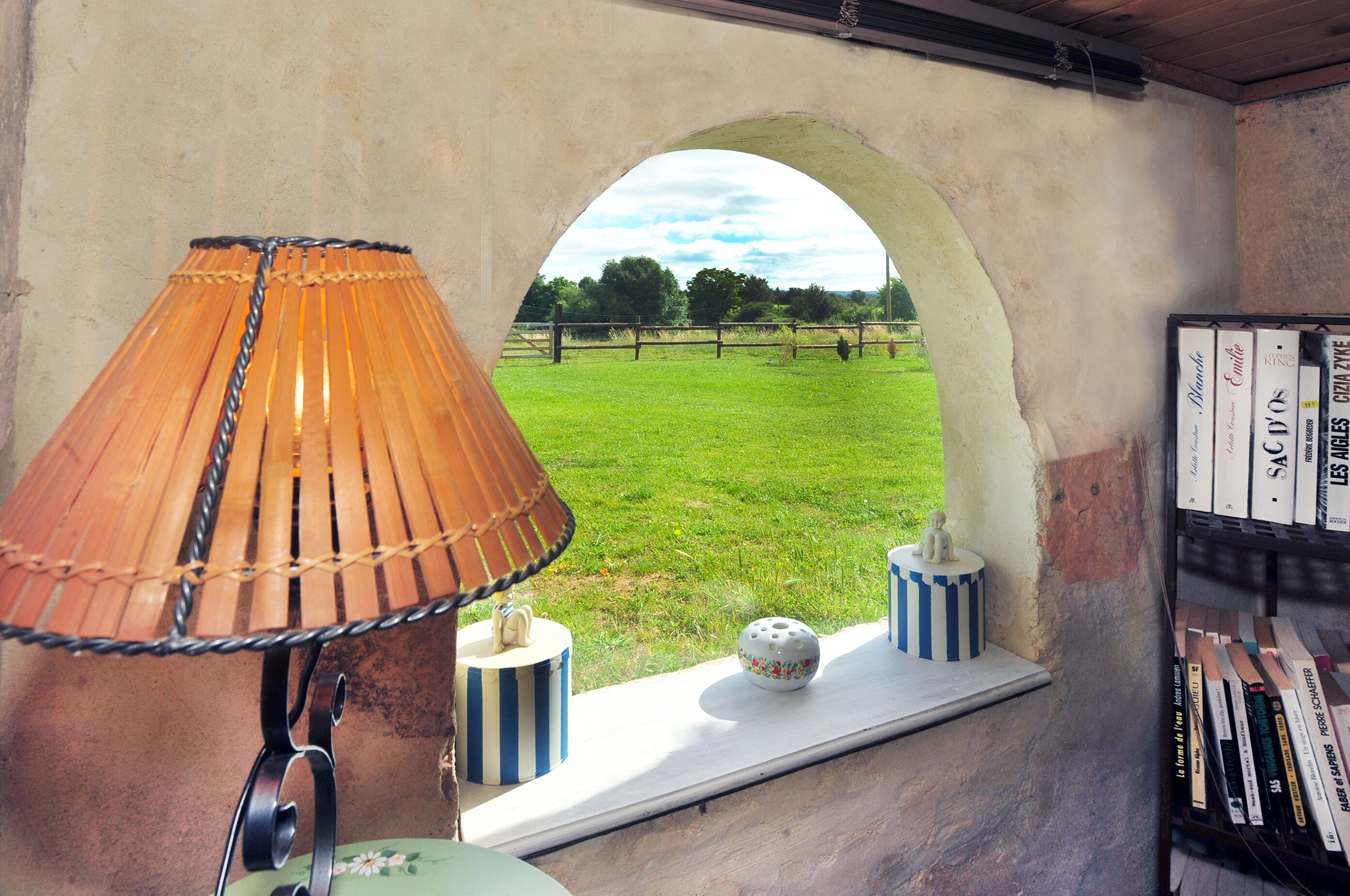 Una habitación con ventana, lámpara, objetos decorativos y una estantería.