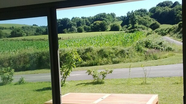 A wooden bench and table on a balcony with a view of a green landscape and a road.