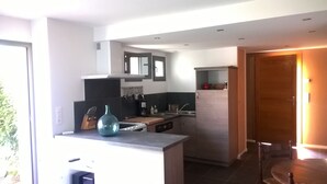 A modern kitchen with a central island, a built-in oven, and a sink. There is a wooden door leading to another room.