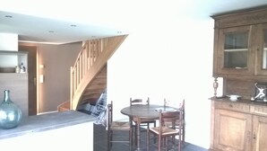 A dining area with a round table and chairs, a wooden staircase, and a kitchen area with cabinets and a sink.