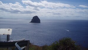 Une vue sur la côte, avec une formation rocheuse imposante qui émerge de la mer, un ciel dégagé et une ligne de rivage lointaine.