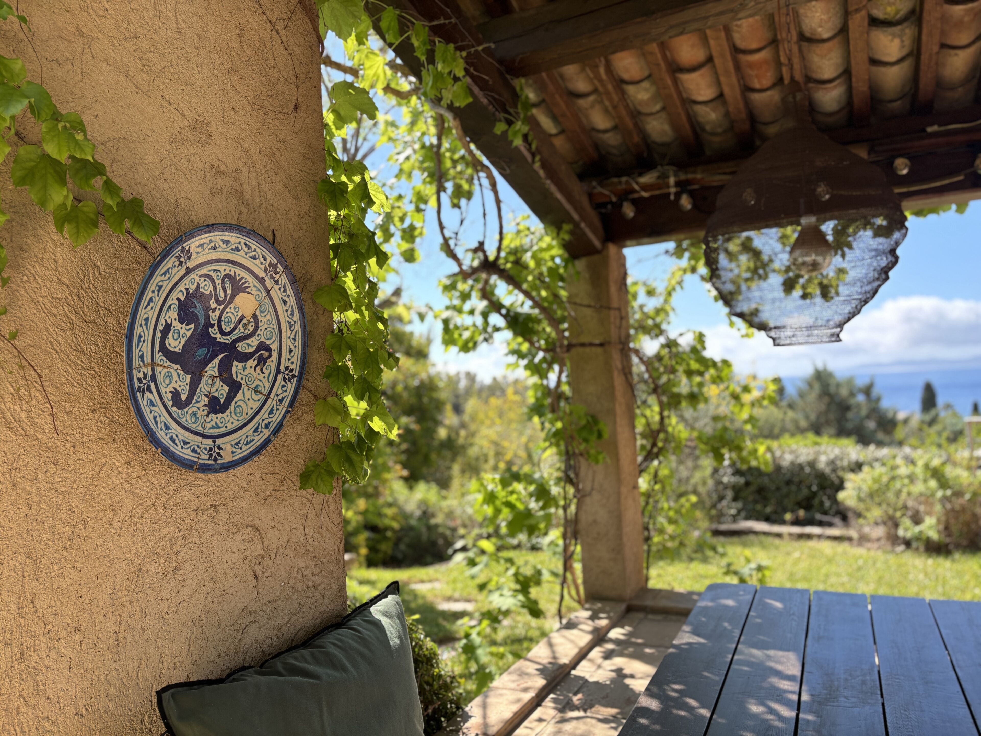 A covered patio with a decorative tile, a wooden bench, and a view of the surrounding garden.