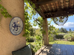 Un patio cubierto con un azulejo decorativo, un banco de madera y vistas al jardín circundante.