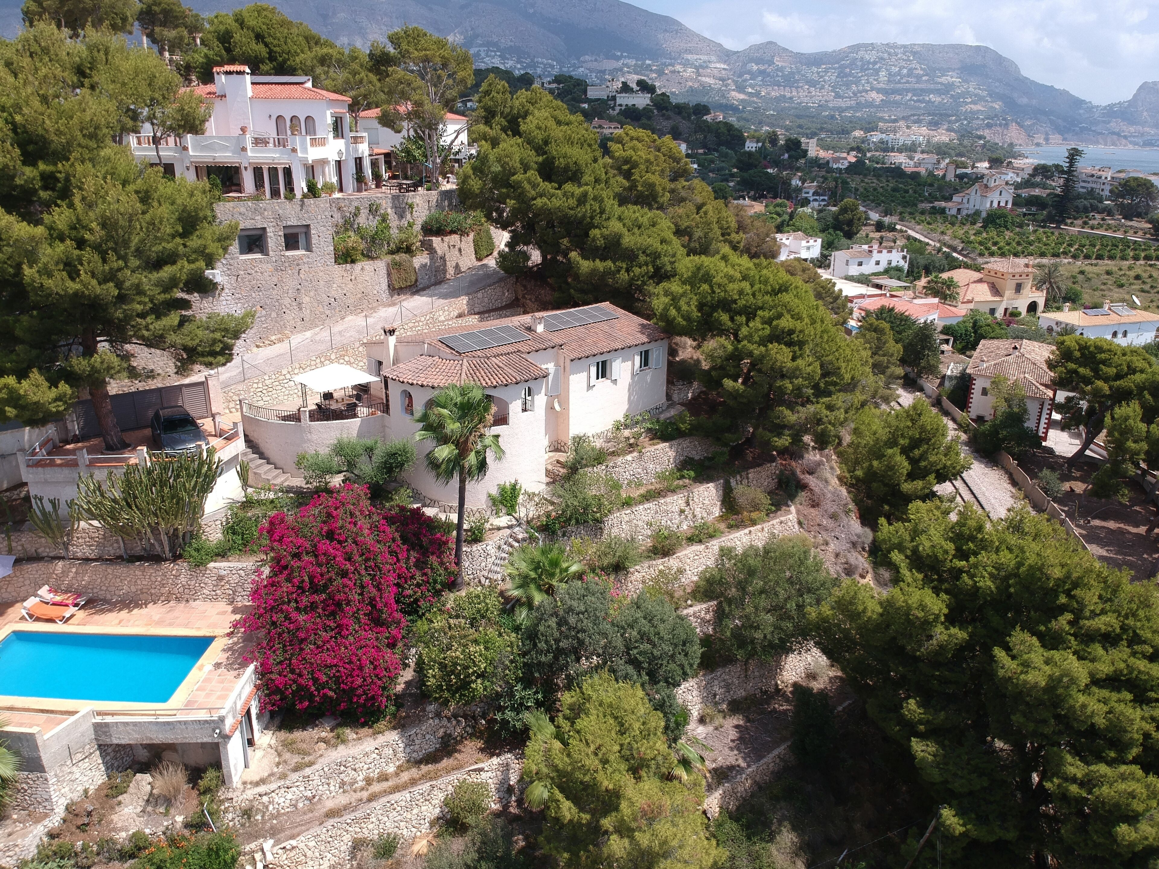 Une villa située sur une colline, dotée d’une piscine, entourée d’une végétation luxuriante et offrant une vue sur la mer.