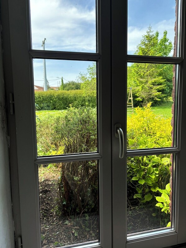 Vista a través de una puerta de cristal con manija metálica, que da a un jardín con diversas plantas y una escalera de fondo.