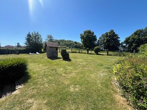 A grassy outdoor area with a small wooden shed, a swing set, and neatly trimmed bushes. - Family gîte with heated indoor pool on the Opal Coast (Tingry)