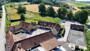 A rural property with multiple buildings, a tennis court, and surrounding fields.