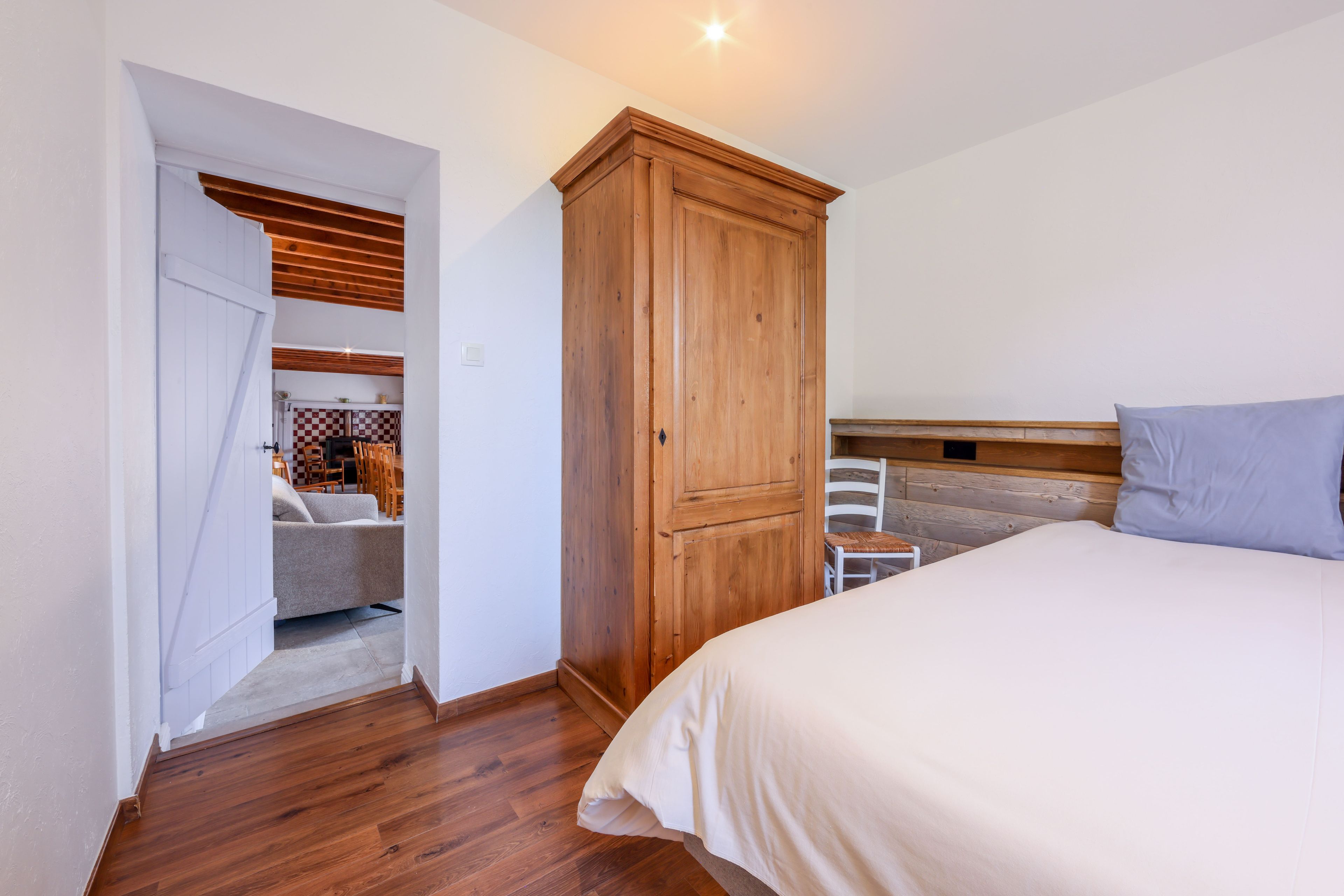A bedroom with a wooden wardrobe, a bed, a chair, and a dining area with chairs and a table.