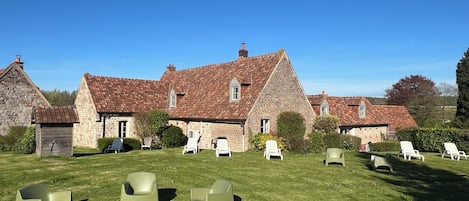 A stone building with a red-tiled roof, surrounded by a grassy lawn with several white lounge chairs.