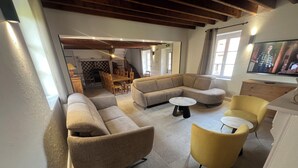 Un salon comprenant un canapé d’angle, des fauteuils jaunes, une table basse ronde et un coin repas avec une table et des chaises en bois.