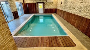 Une piscine intérieure dotée d’une terrasse en bois, de murs en pierre et d’une porte donnant sur l’extérieur.