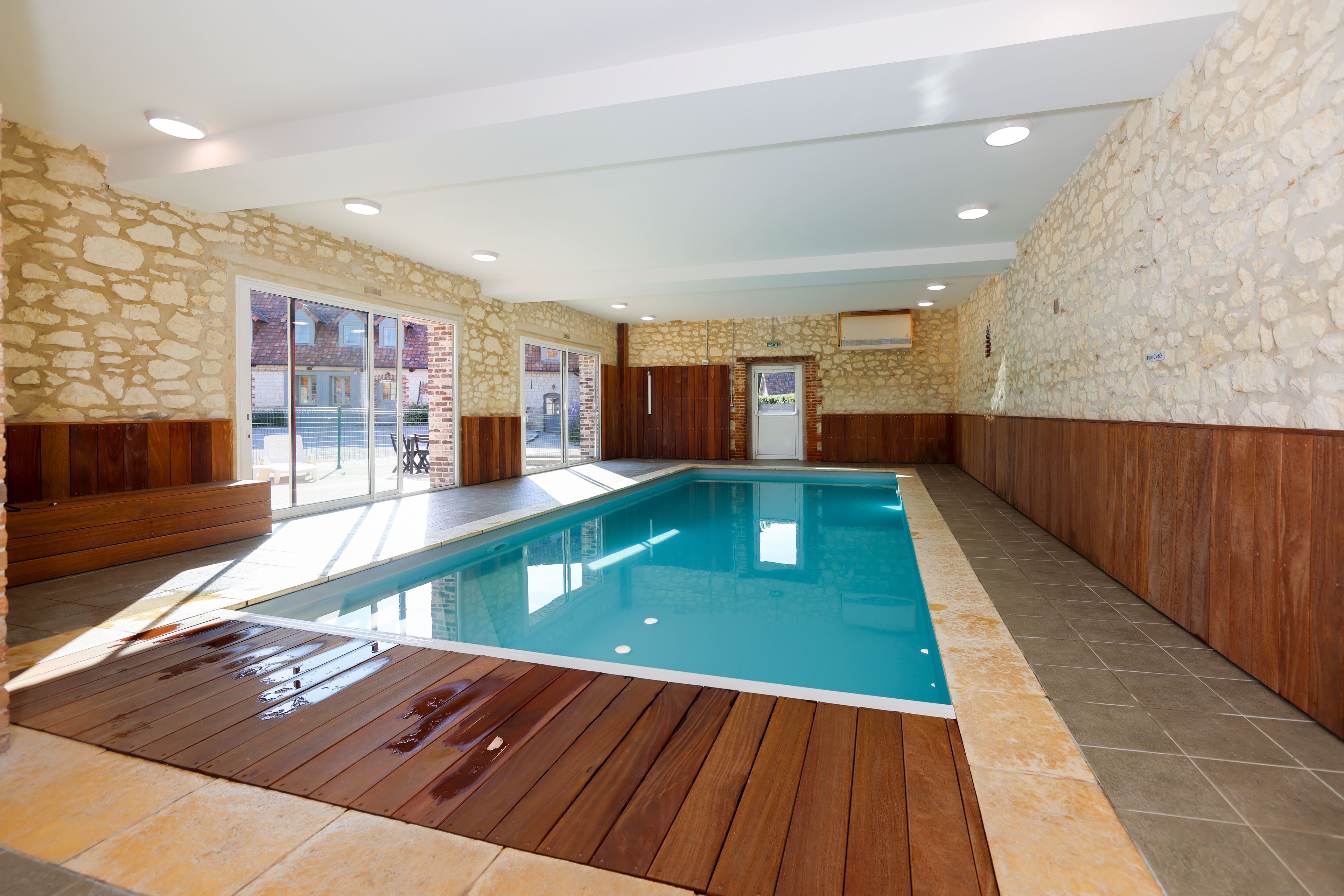 An indoor swimming pool with stone walls, wooden benches, and a tiled floor.