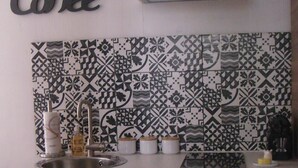 A kitchen with a stainless steel sink, a coffee sign, patterned backsplash, and a doormat with city names. - Grand T1 in hyper-center in a classified building (Dijon)