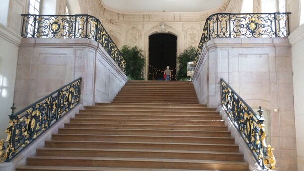 A grand staircase with ornate black and gold railings, leading to a dark doorway. - Grand T1 in hyper-center in a classified building (Dijon)