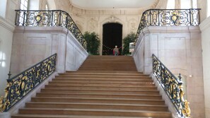 A grand staircase with ornate black and gold railings, leading to a dark doorway.