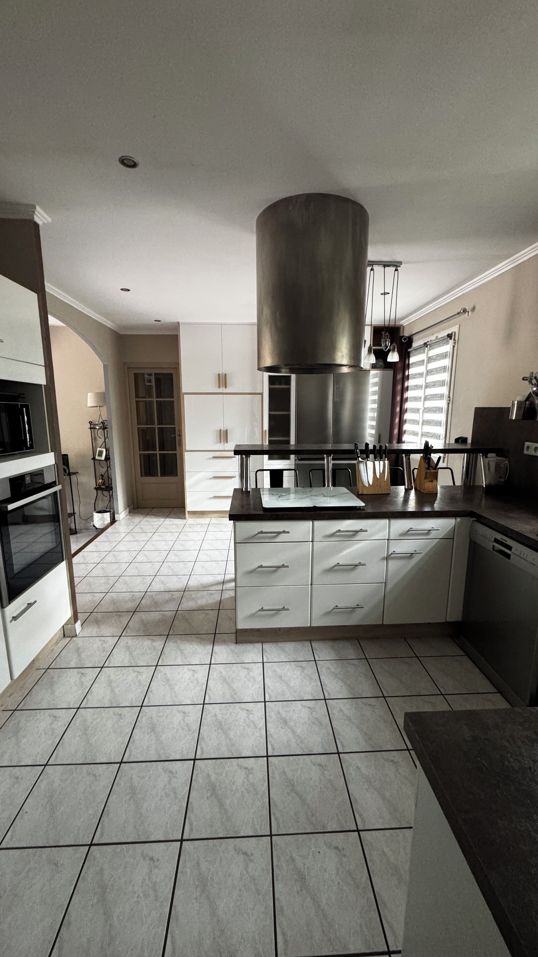 A modern kitchen with white cabinetry, a stainless steel range hood, and a central island with a marble countertop.