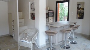 A kitchen with a bar area, white wicker chairs, a white refrigerator, and a clock on the wall. - Charming maisonette ****, Pool with sea view, Golf, Spa, Quiet, Open spaces (Bouches-du-Rhône)