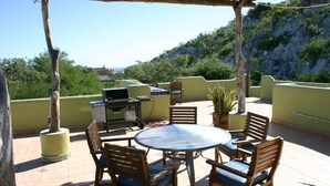 Un patio al aire libre con una mesa redonda y sillas, una parrilla y una planta en maceta.