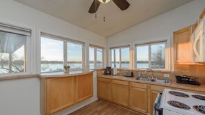 A kitchen with wooden cabinets, a stove, a sink, and large windows overlooking a body of water.
