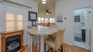 A kitchen with a round table, wicker chairs, a ceiling fan, and a view of the bathroom through an open door.