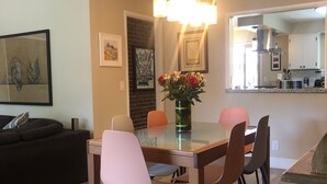 A dining area with a glass table, four chairs, a vase with flowers, and a hanging light fixture. - Chico Family Retreat with Pool~Bocce~Hot-tub~Lounge. Near park, downtown & CSU (Chico)