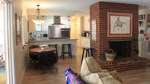 A modern kitchen with a central island, a dining area with a round table, and a brick fireplace. - Chico Family Retreat with Pool~Bocce~Hot-tub~Lounge. Near park, downtown & CSU (Chico)