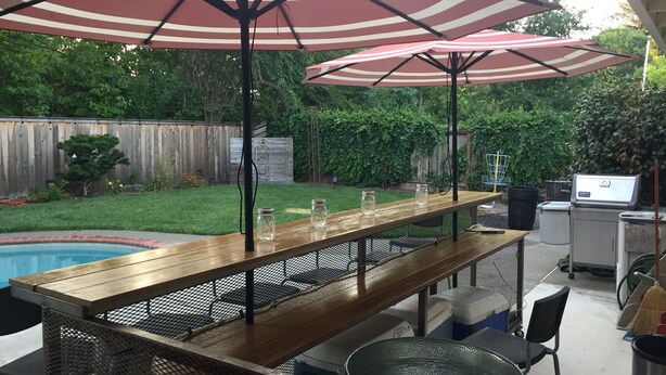 An outdoor patio with a wooden table, metal chairs, and two striped umbrellas. - Chico Family Retreat with Pool~Bocce~Hot-tub~Lounge. Near park, downtown & CSU (Chico)