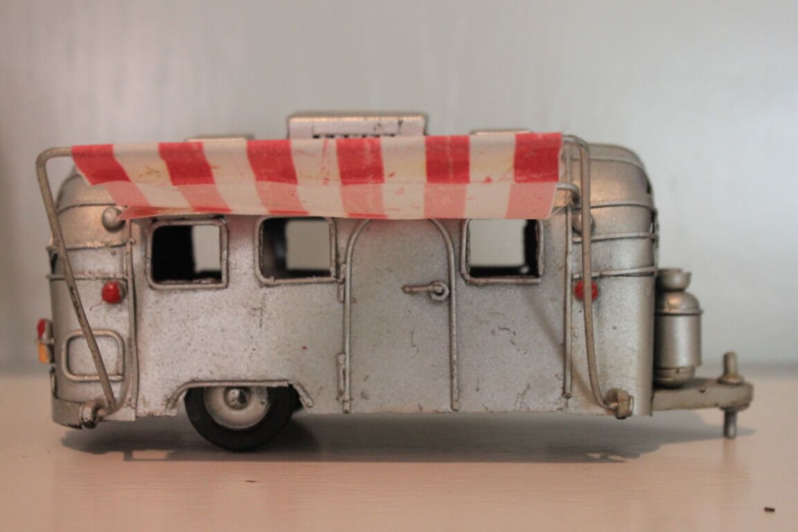 A vintage model train with a red and white checkered awning, a small window, and a cylindrical tank on the side.