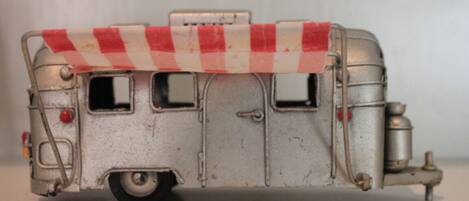 A vintage model train with a red and white checkered awning, a small window, and a cylindrical tank on the side.