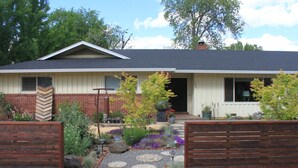 A single-story house with a brick facade, a front porch with a bench, and a garden with various plants and a gravel pathway. - Chico Family Retreat with Pool~Bocce~Hot-tub~Lounge. Near park, downtown & CSU (Chico)