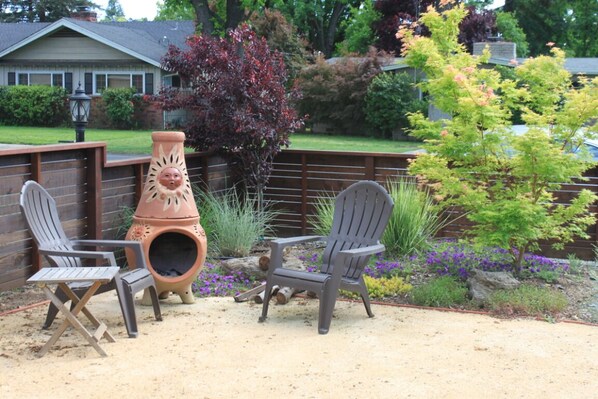 A patio area with two Adirondack chairs, a decorative clay pot, and a small tree.